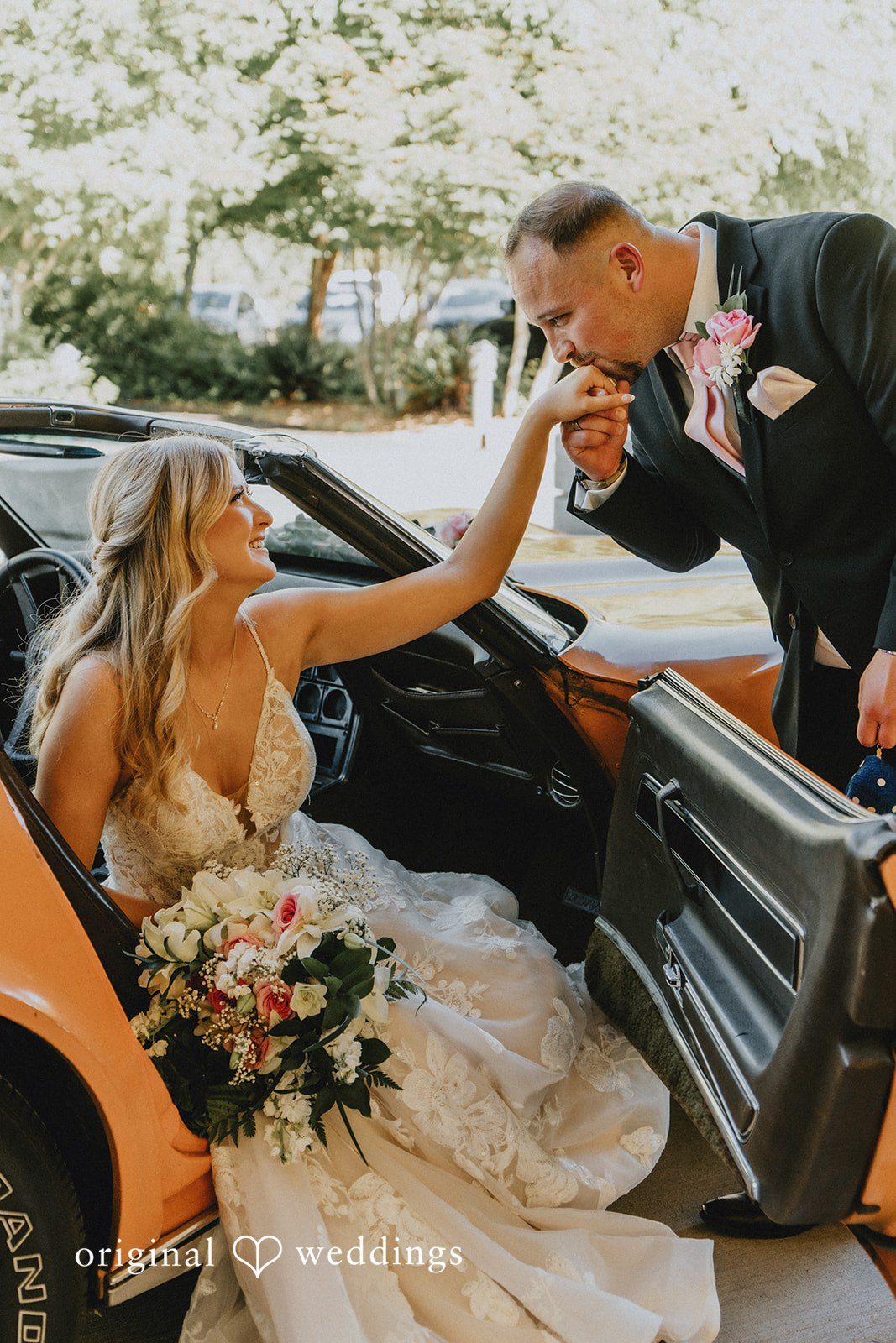 Ashley + Dylan A bride sitting inside an orange convertible sports car while leaning back toward her groom.