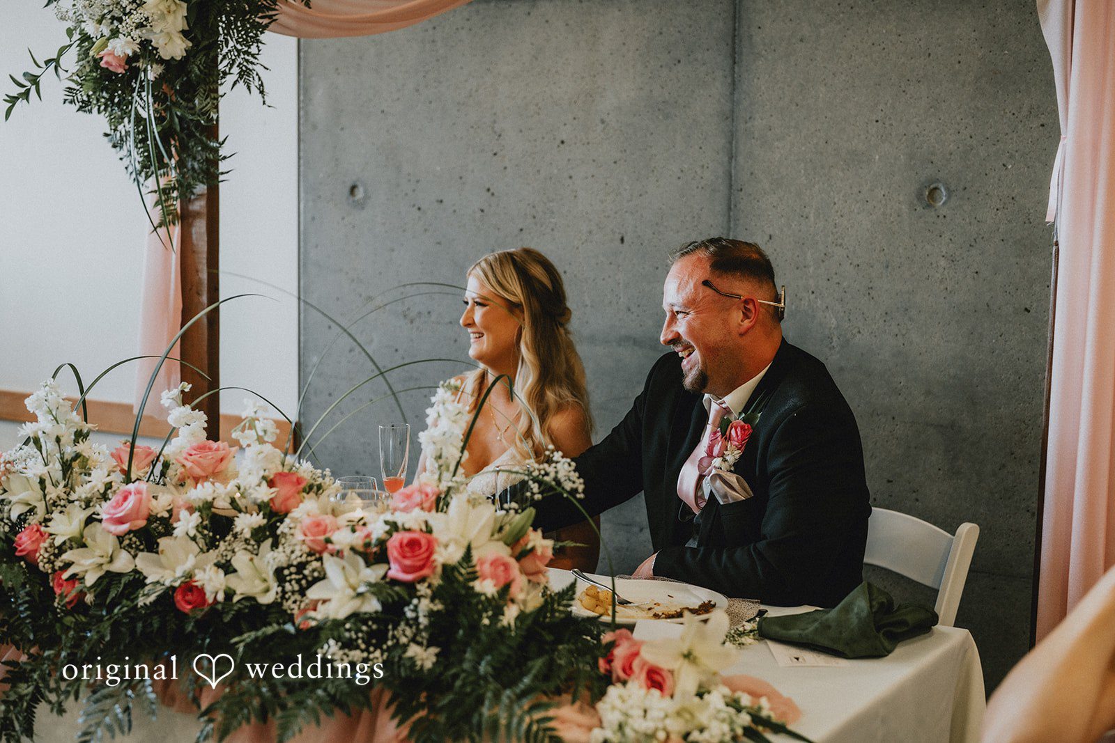 Ashley + Dylan A bride and groom sitting at a decorated sweetheart table during their wedding reception.