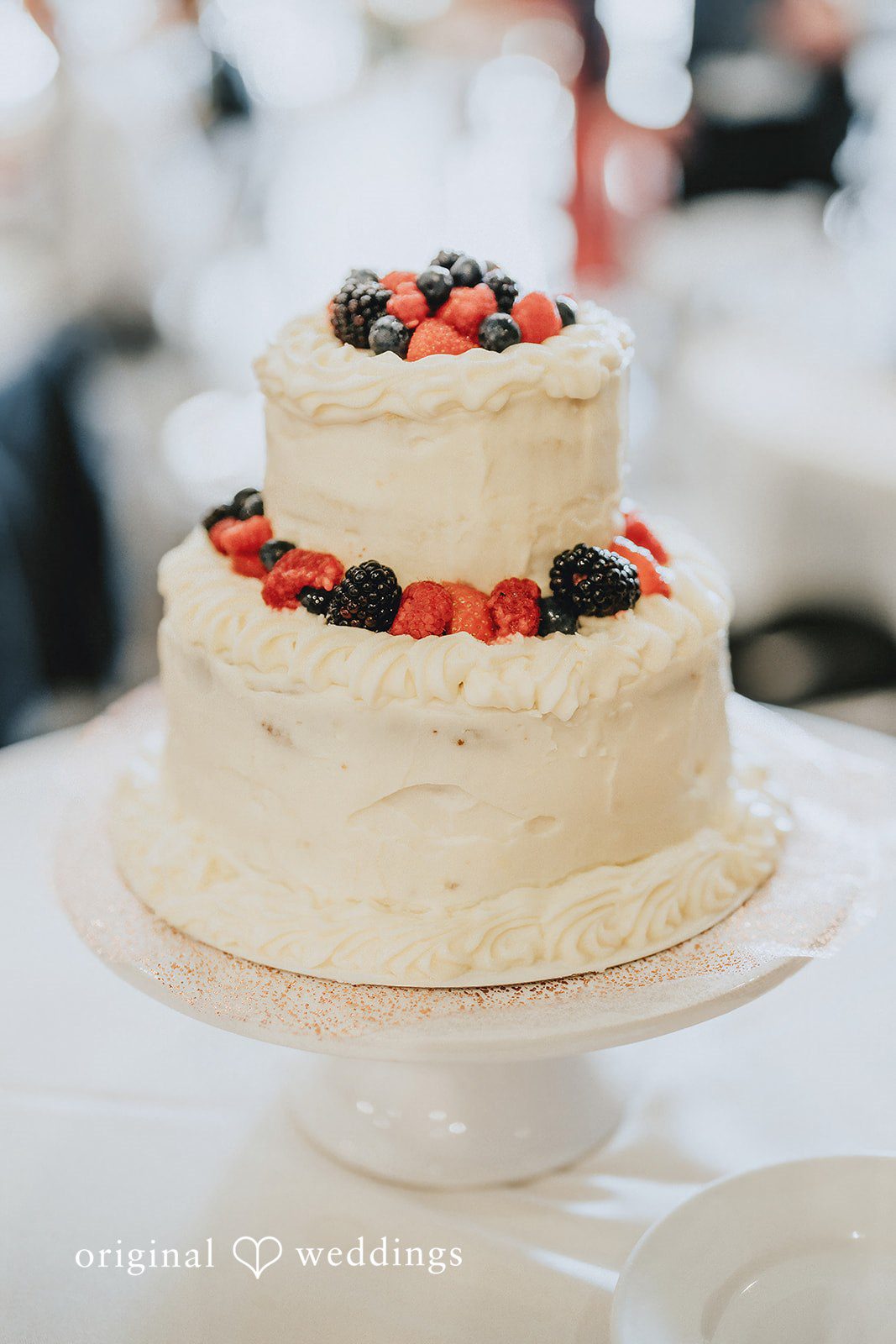 Ashley + Dylan A three-tiered white wedding cake decorated with fresh berries on a stand.