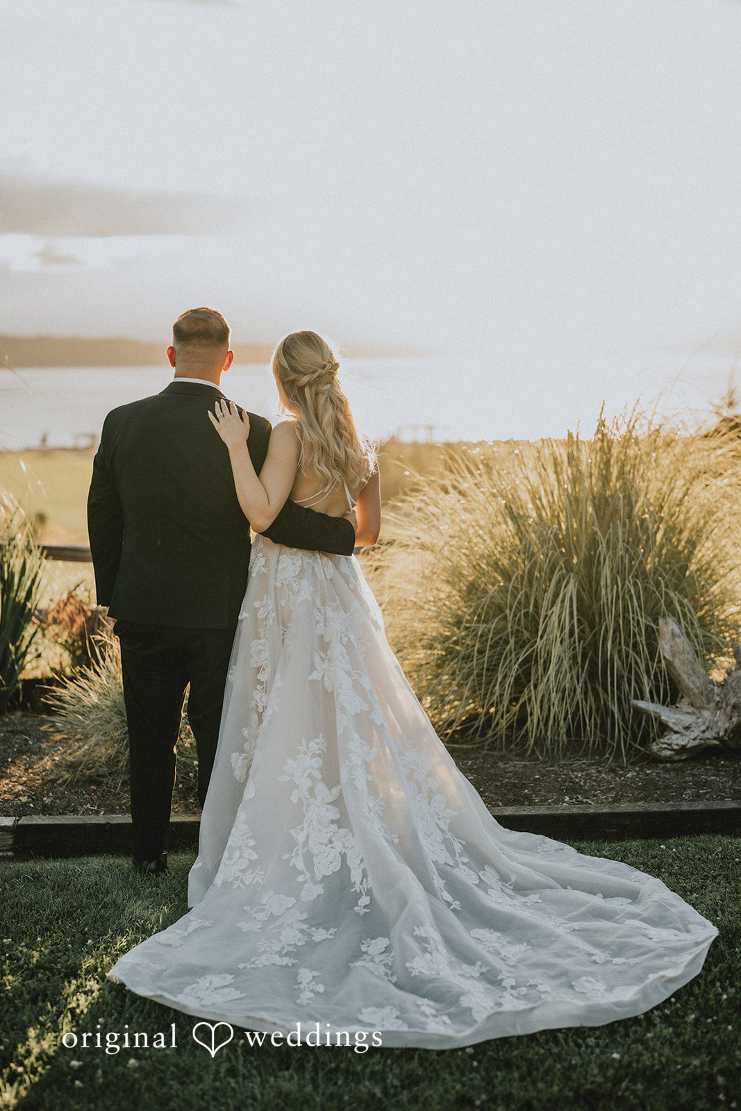 Ashley + Dylan A bride and groom walking hand-in-hand through a sunlit field with tall grass.
