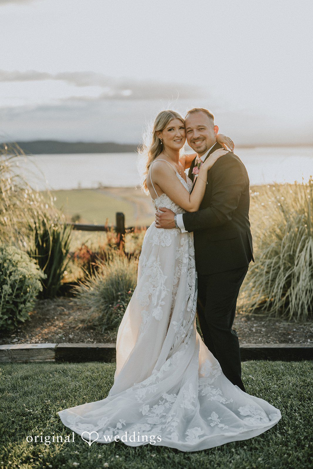 Ashley + Dylan A bride and groom sharing a romantic embrace in a field during a golden hour sunset.