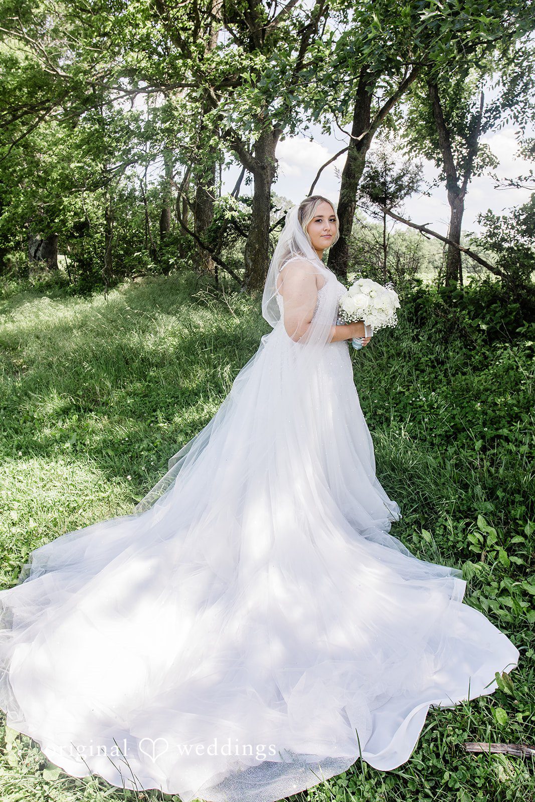 A bride in a large gown with a long train walking across a grassy field.
