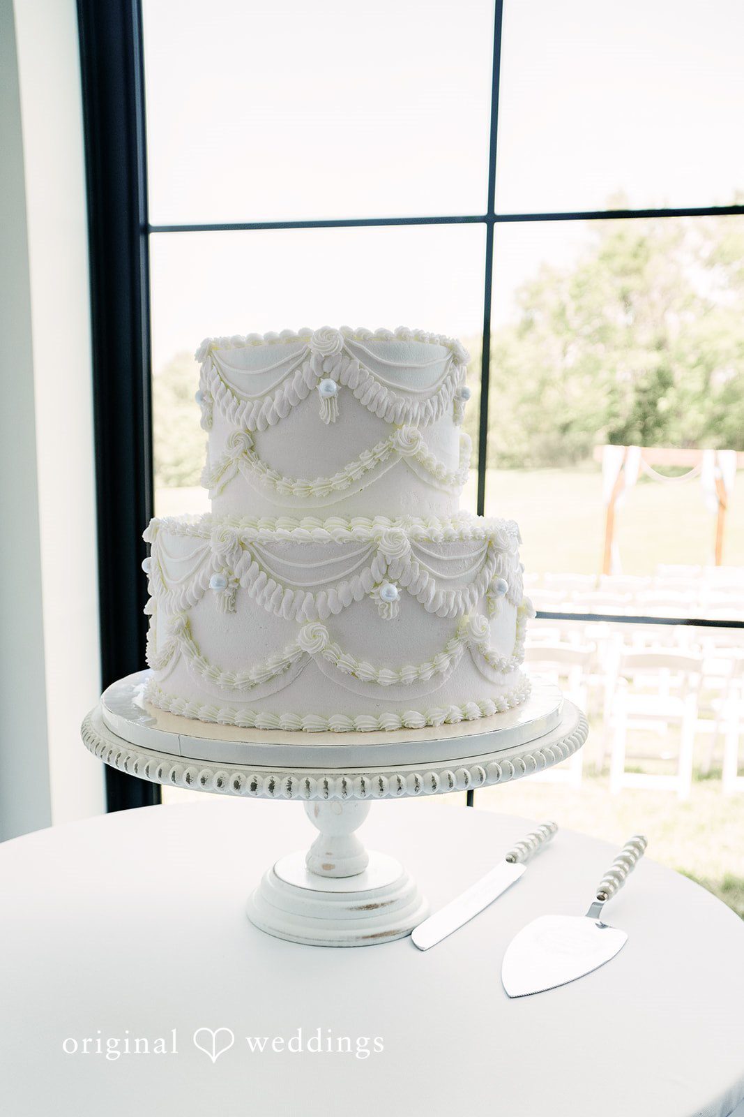 A multi-tiered white wedding cake decorated with delicate floral patterns displayed on a pedestal stand.