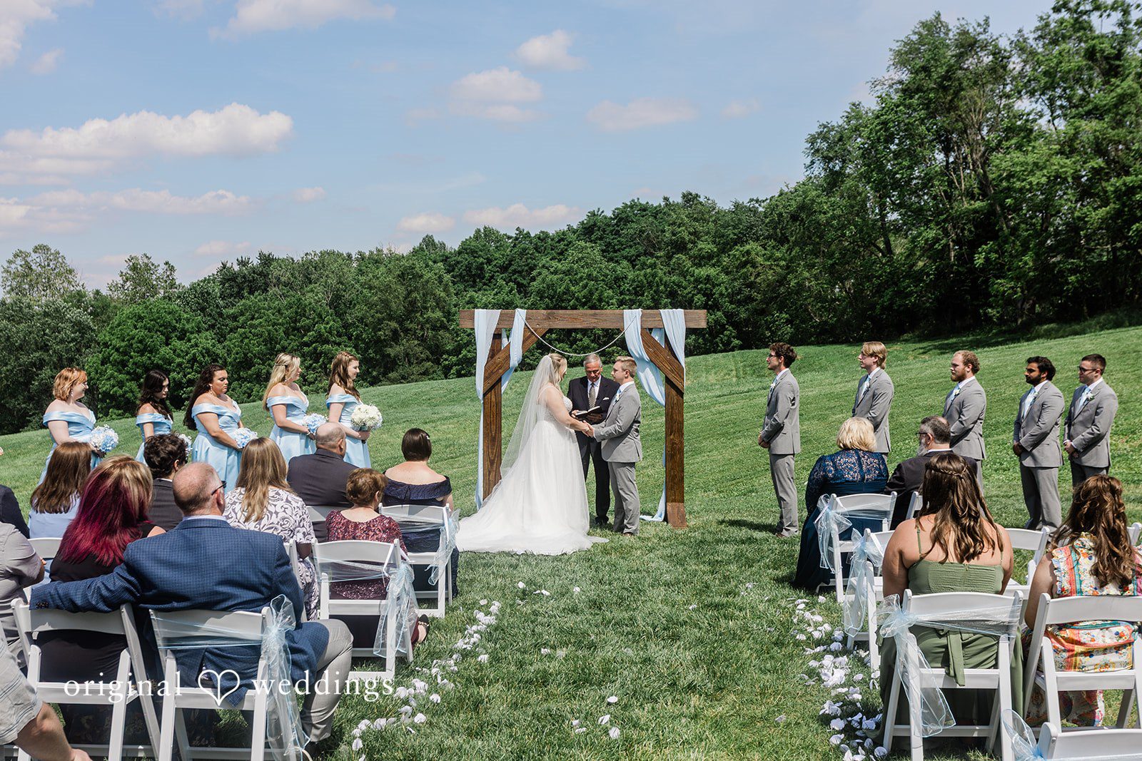 An open-air wedding ceremony setup with rows of white chairs facing a rustic wooden altar.
