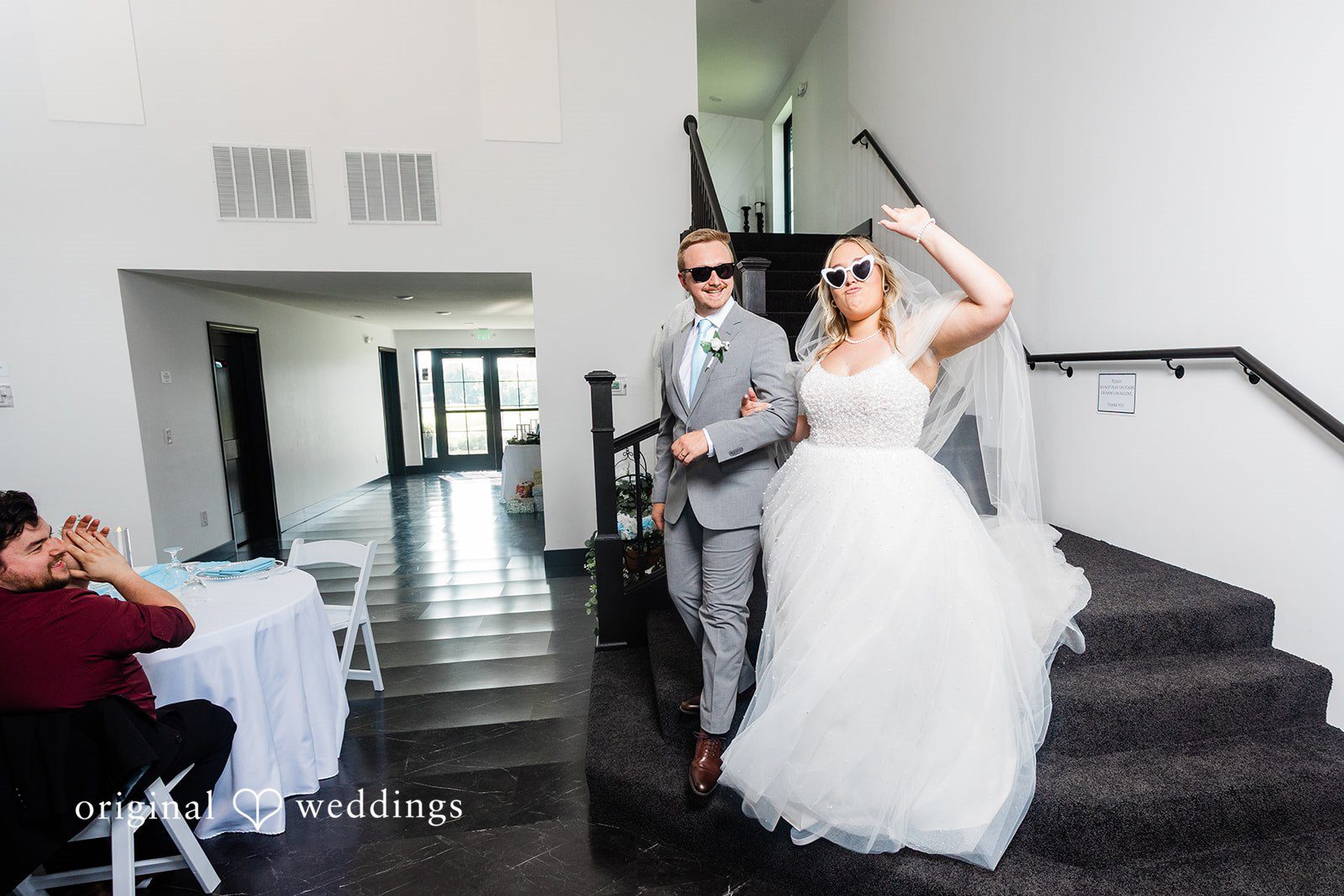A bride and groom wearing sunglasses walk down a dark staircase while making a grand entrance at their wedding reception.