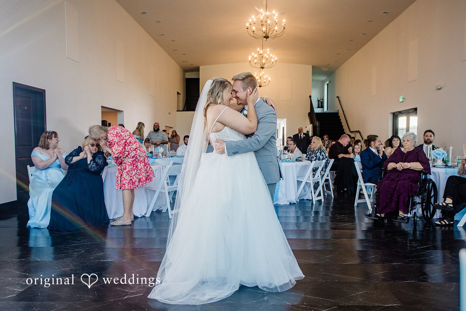 A bride and groom sharing a dance together in the center of a rustic hall.