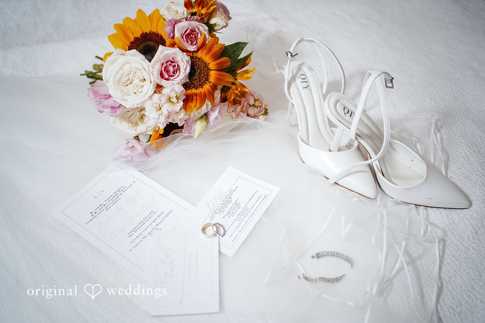 Vincenzo + Kristin A flat lay of wedding details including a bouquet, bridal shoes, and invitations.
