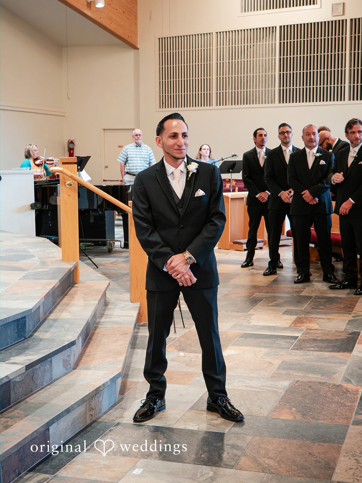 Vincenzo + Kristin A groom in a black suit standing on a staircase during the wedding event.