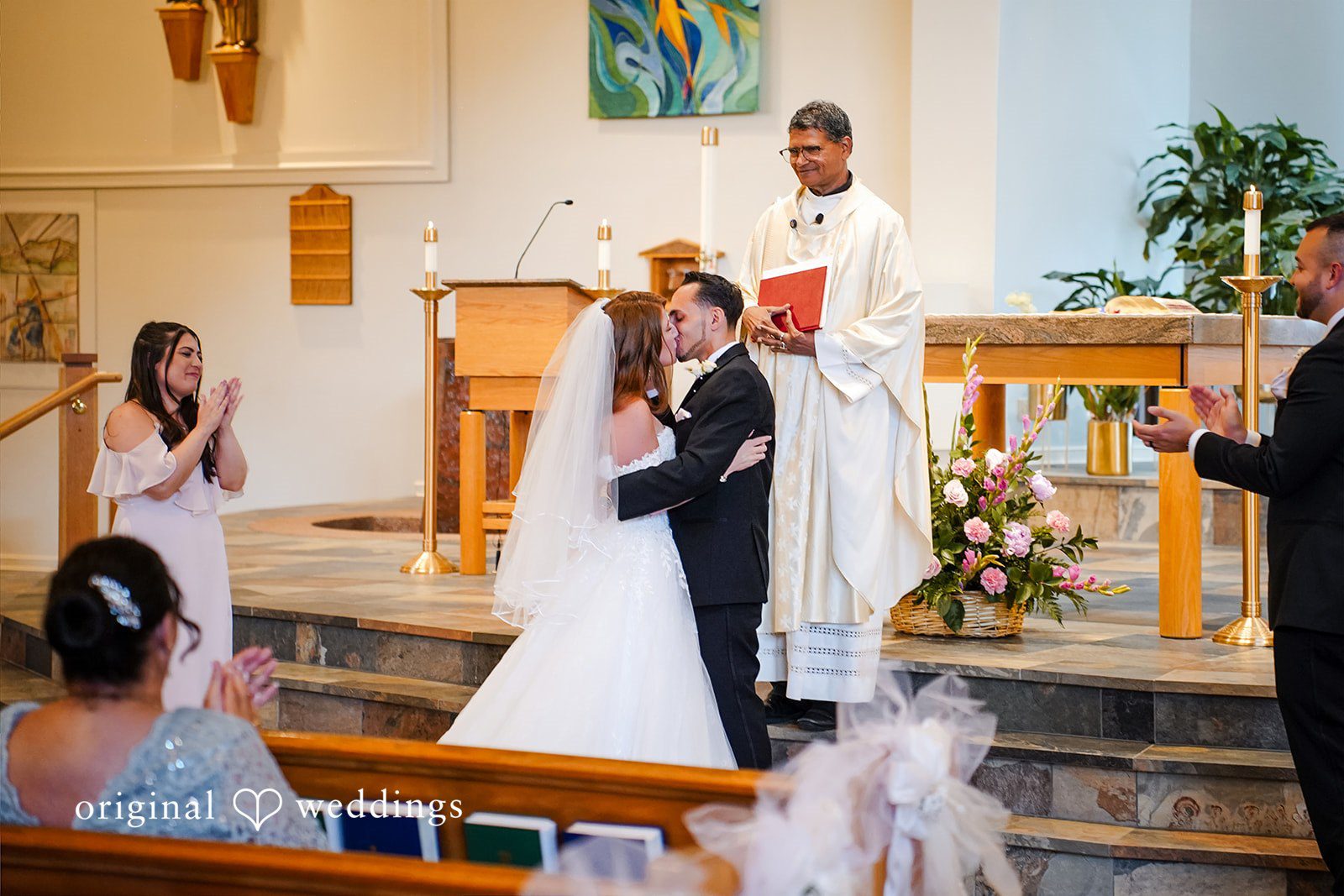 Vincenzo + Kristin A wedding ceremony kissing each other and taking place inside a church filled with guests.