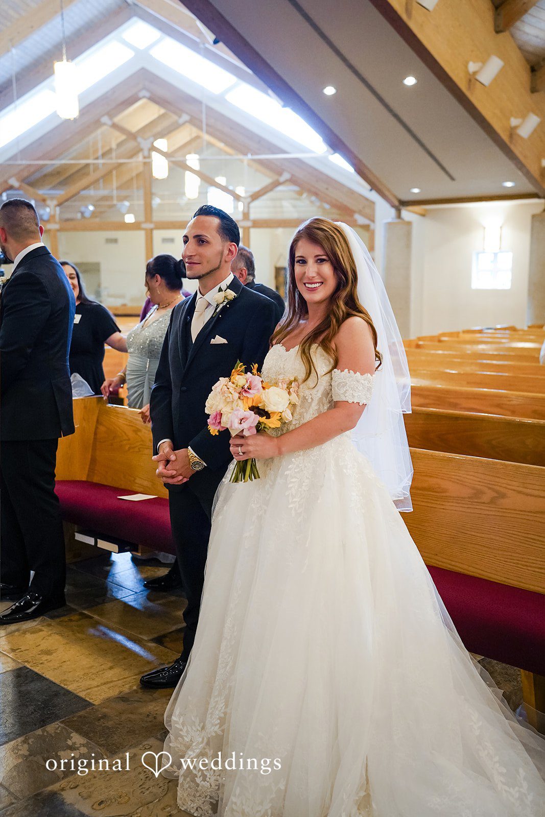Vincenzo + Kristin A bride in an off-the-shoulder white gown holding a bouquet and a groom in a dark suit stand together