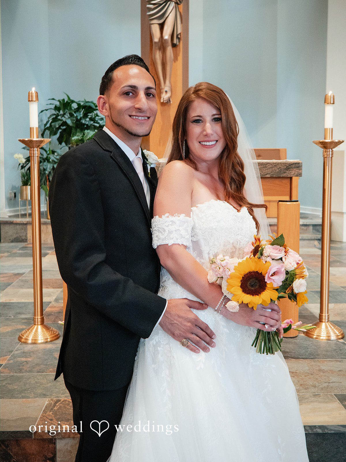 Vincenzo + Kristin A smiling bride holding a sunflower bouquet poses with her groom