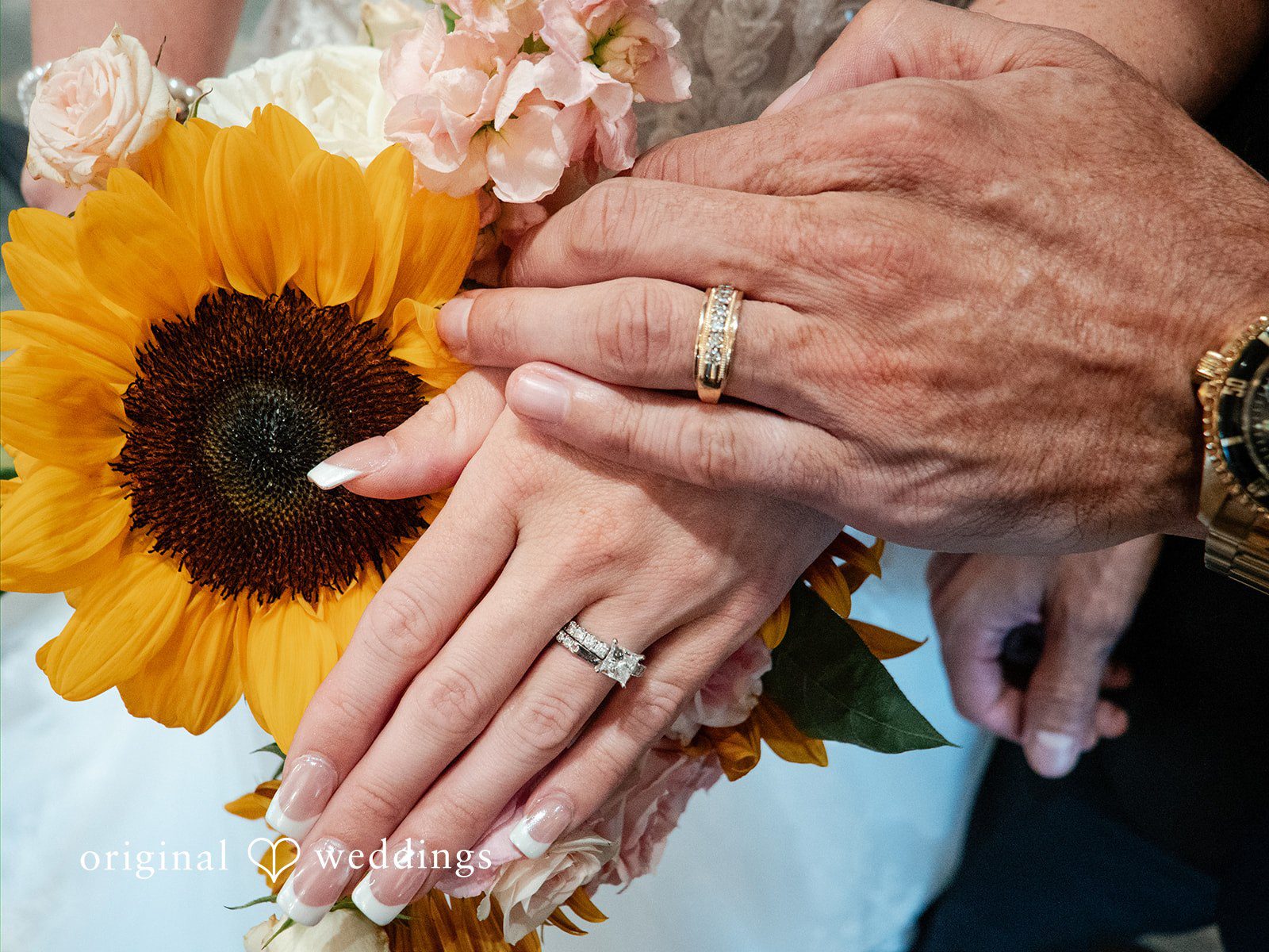 Vincenzo + Kristin A close-up of a bride showing her wedding rings next to a sunflower bouquet.