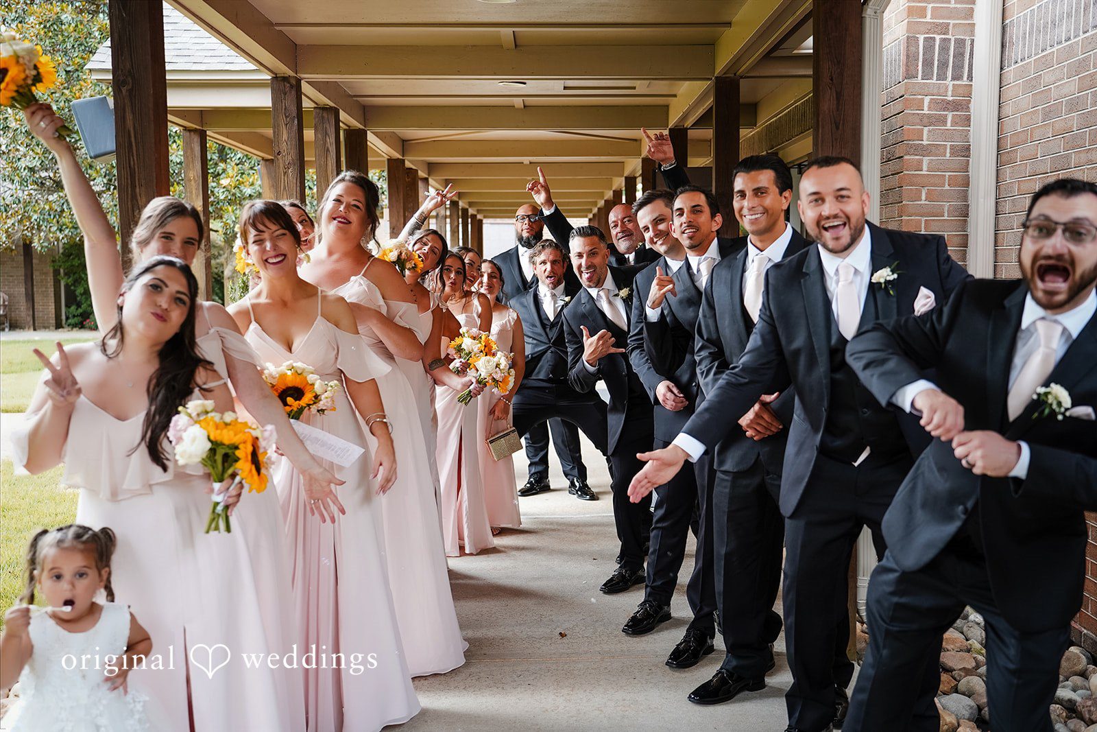Vincenzo + Kristin A large wedding party of bridesmaids and groomsmen posing in a decorated hallway.
