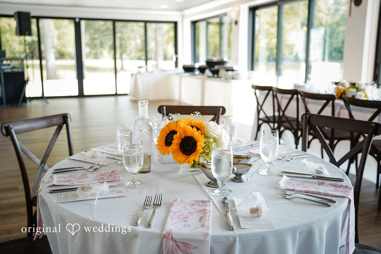 Vincenzo + Kristin A round reception table set with white plates, wine glasses, and floral centerpieces.