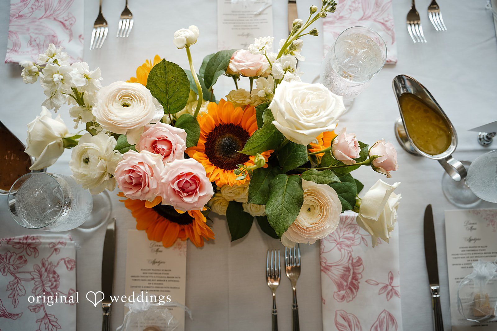 Vincenzo + Kristin A close-up of a floral centerpiece featuring bright sunflowers and white roses.