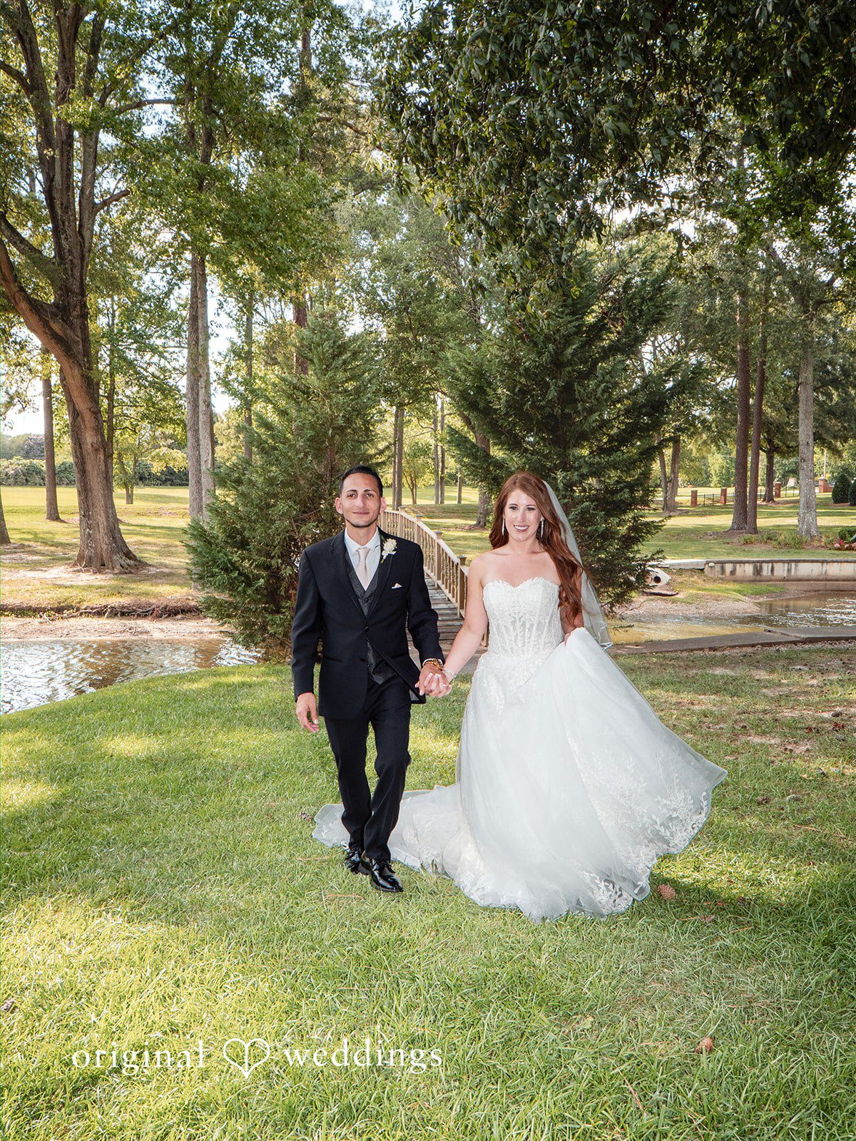 Vincenzo + Kristin A bride and groom walking down a scenic path together in a grassy field.
