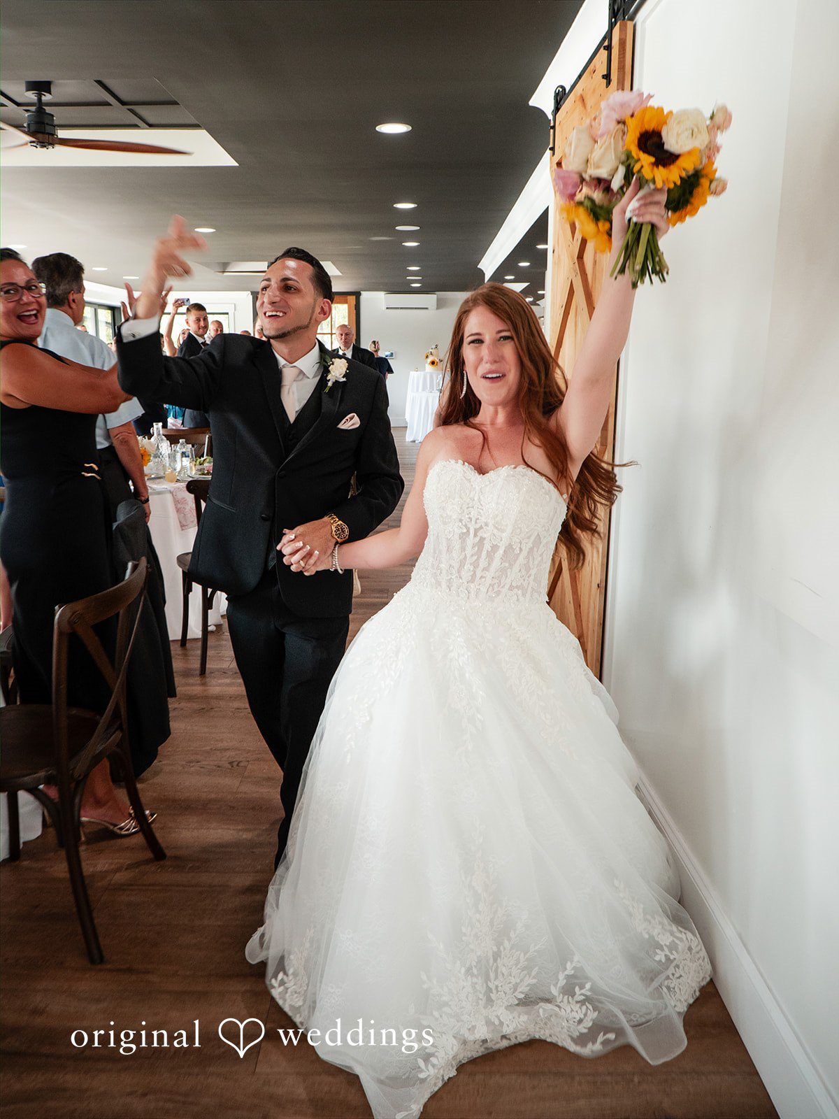 Vincenzo + Kristin A bride and groom smiling as they walk through a rustic aisle lined with guests.