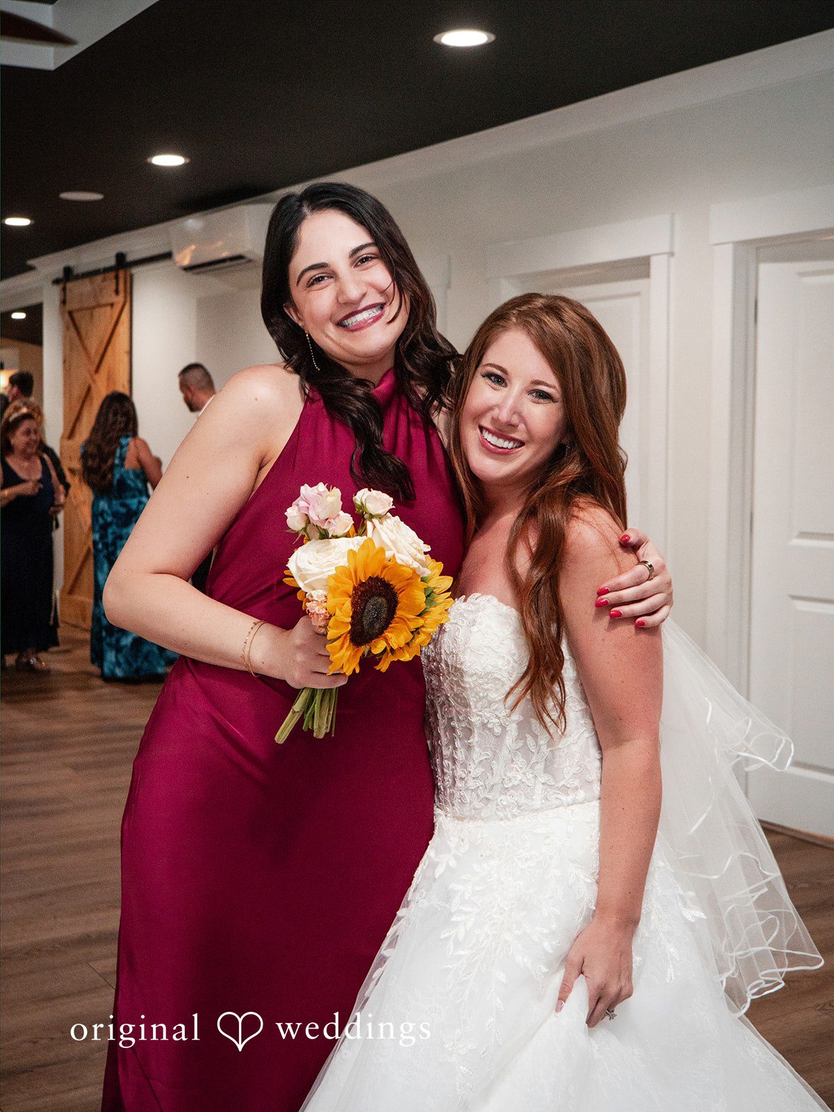 Vincenzo + Kristin A bride smiling alongside a bridesmaid in a maroon dress.