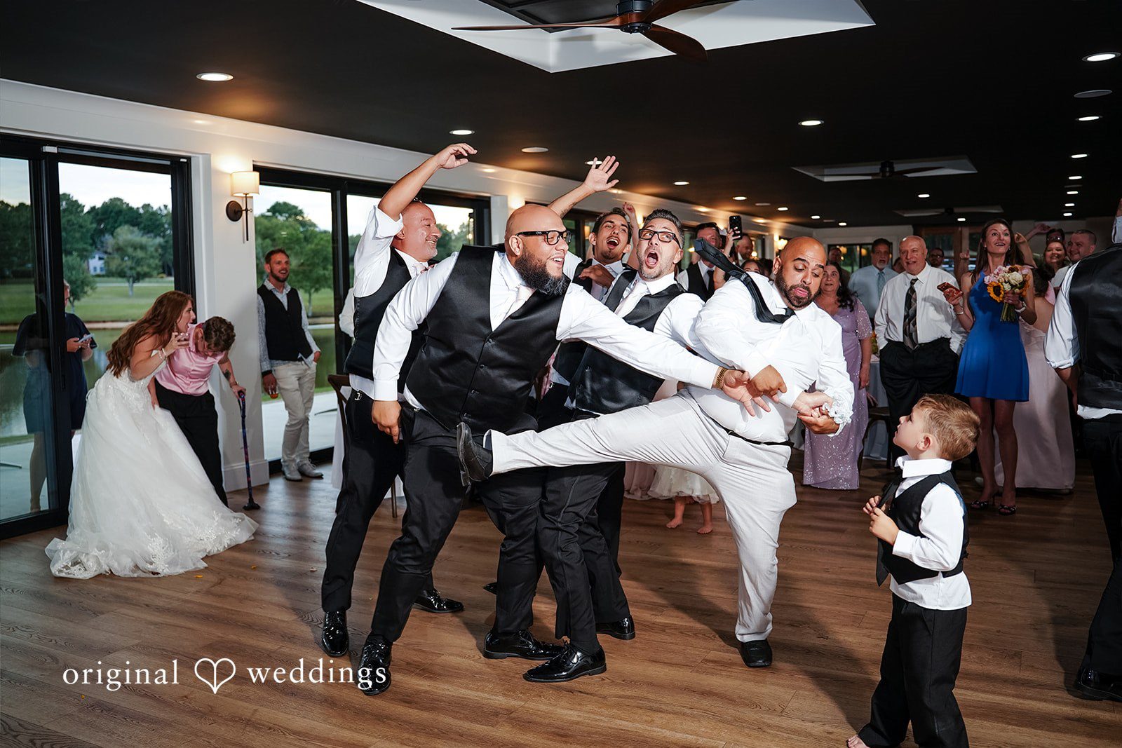 Vincenzo + Kristin A group of wedding guests dancing and celebrating together on a crowded dance floor.