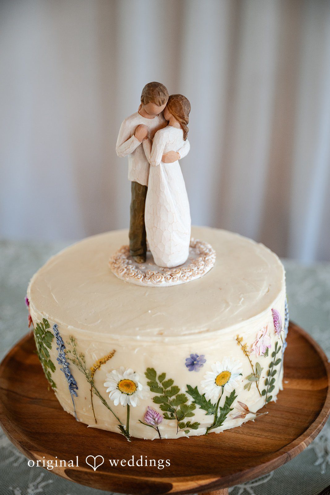 Emma + Aidan A white frosted wedding cake topped with a small bride and groom figurine.