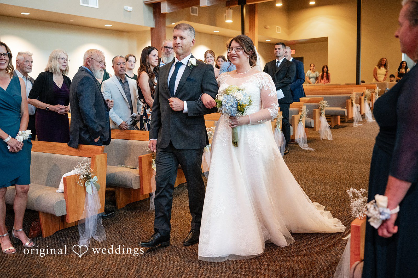 Emma + Aidan A bride walking down the church aisle surrounded by wedding guests.