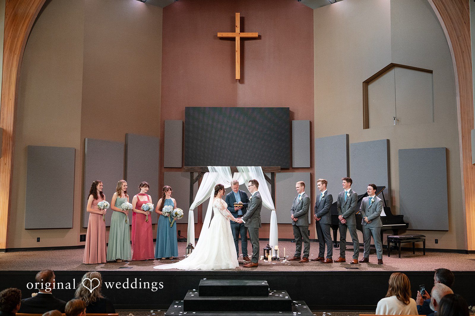 Emma + Aidan A wedding ceremony taking place on a stage with a dark fabric backdrop.