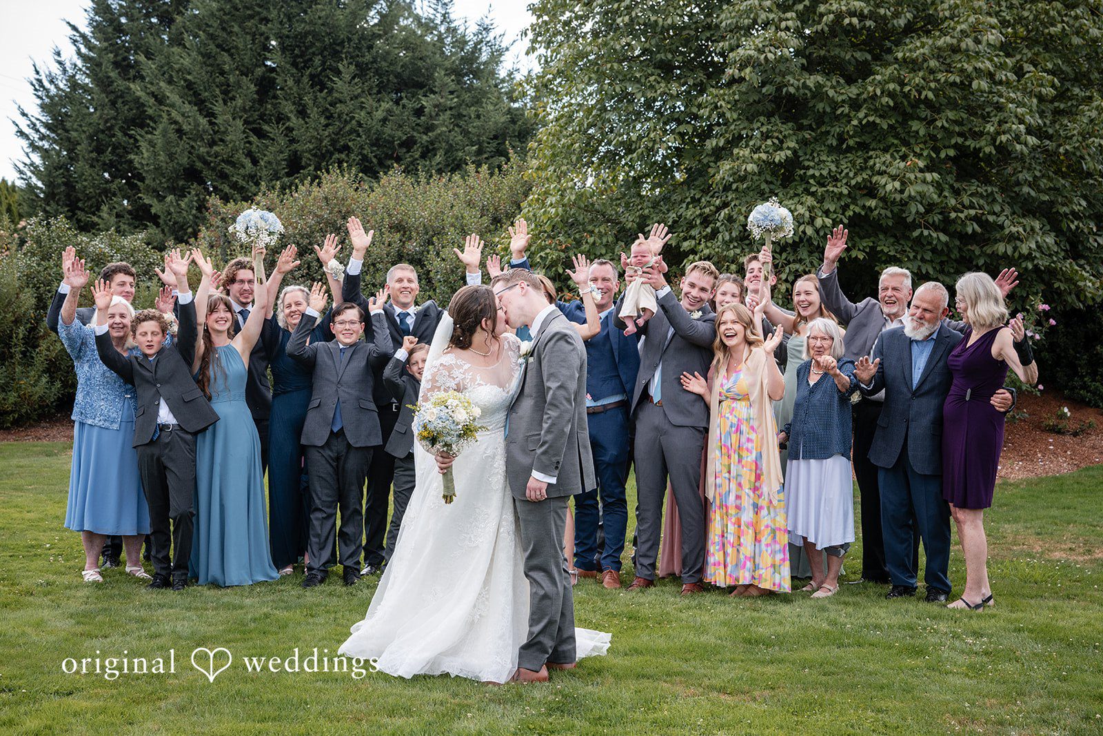 Emma + Aidan A large group of wedding guests cheering with raised hands behind a bride and groom.