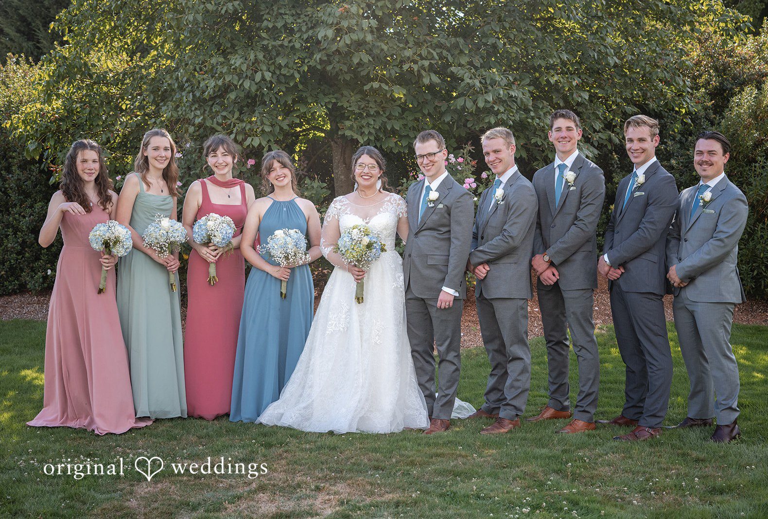 A full wedding party consisting of bridesmaids and groomsmen posing together in a line at The Old Schoolhouse by Portland Wedding Photographers from Original Weddings..