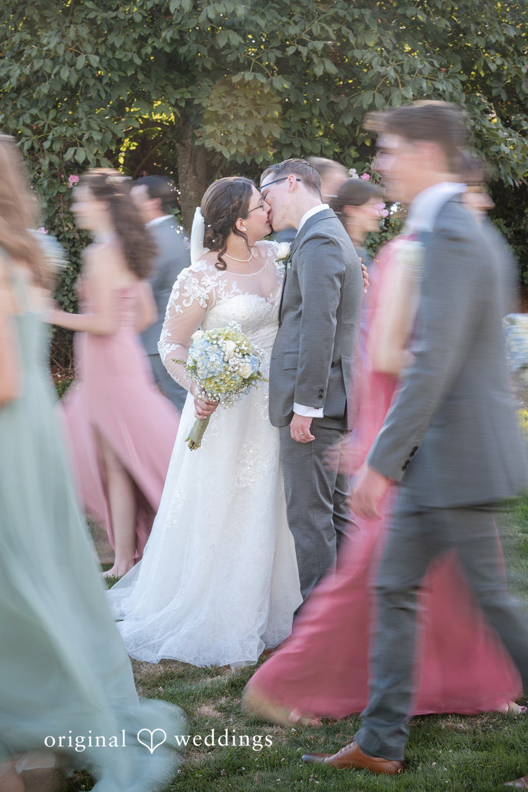 Emma + Aidan A blurred action shot of a bride, groom, and wedding guests moving outdoors.