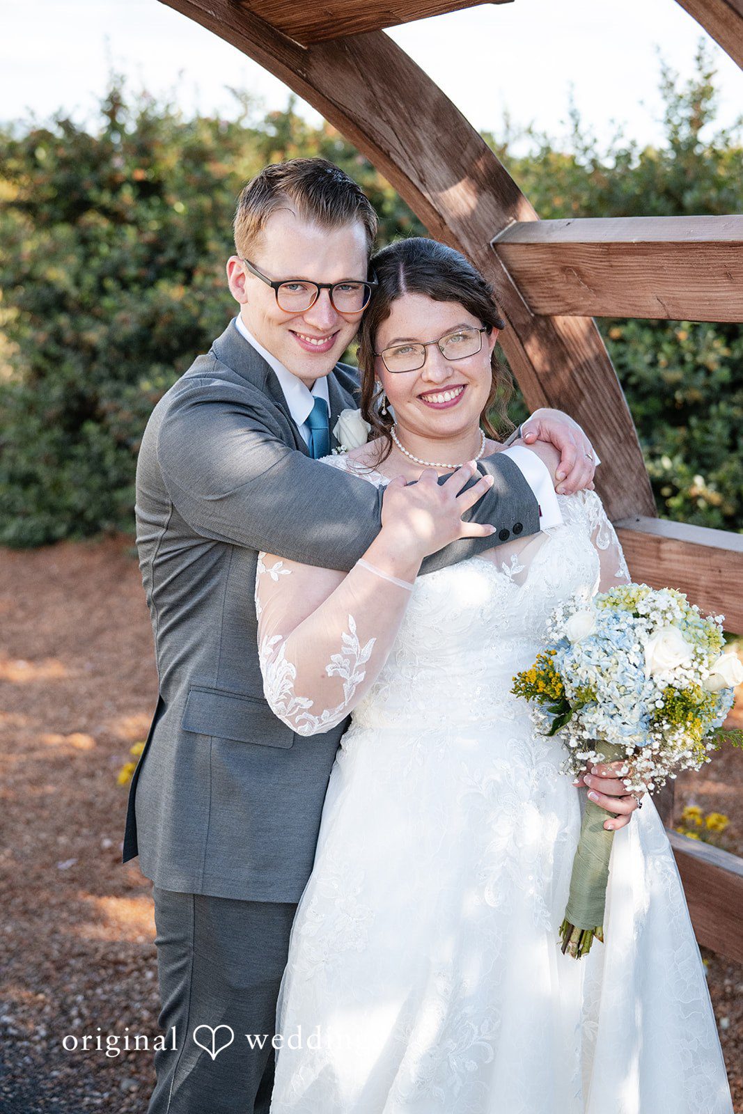 Emma + Aidan A bride and groom smiling together while posing near a wooden fence.