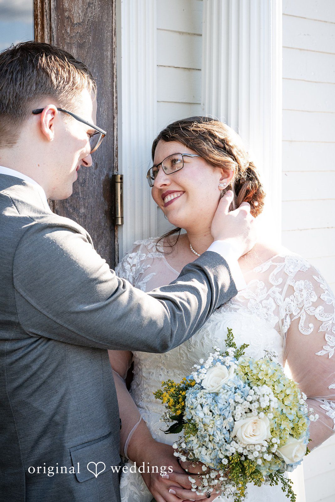 Emma + Aidan A groom looking lovingly at his smiling bride as she holds a blue bouquet.