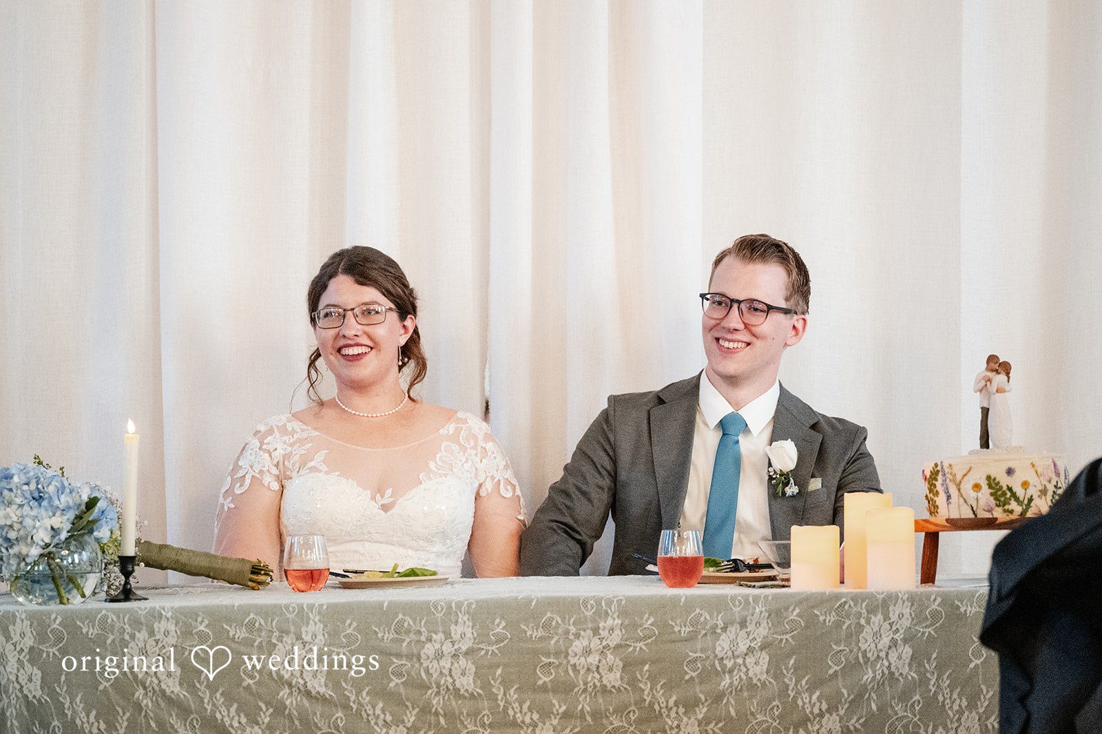 Emma + Aidan A bride and groom sitting together at a decorated head table during their reception.