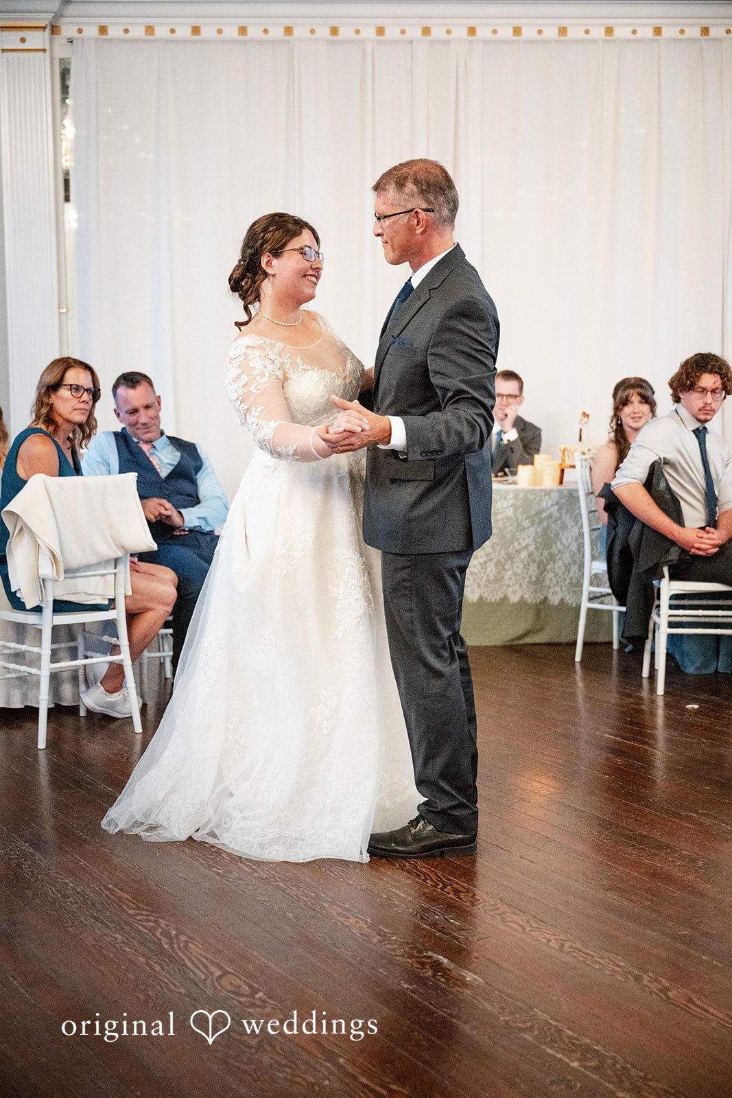 Emma + Aidan A bride and man sharing a dance on a wooden floor surrounded by seated guests.