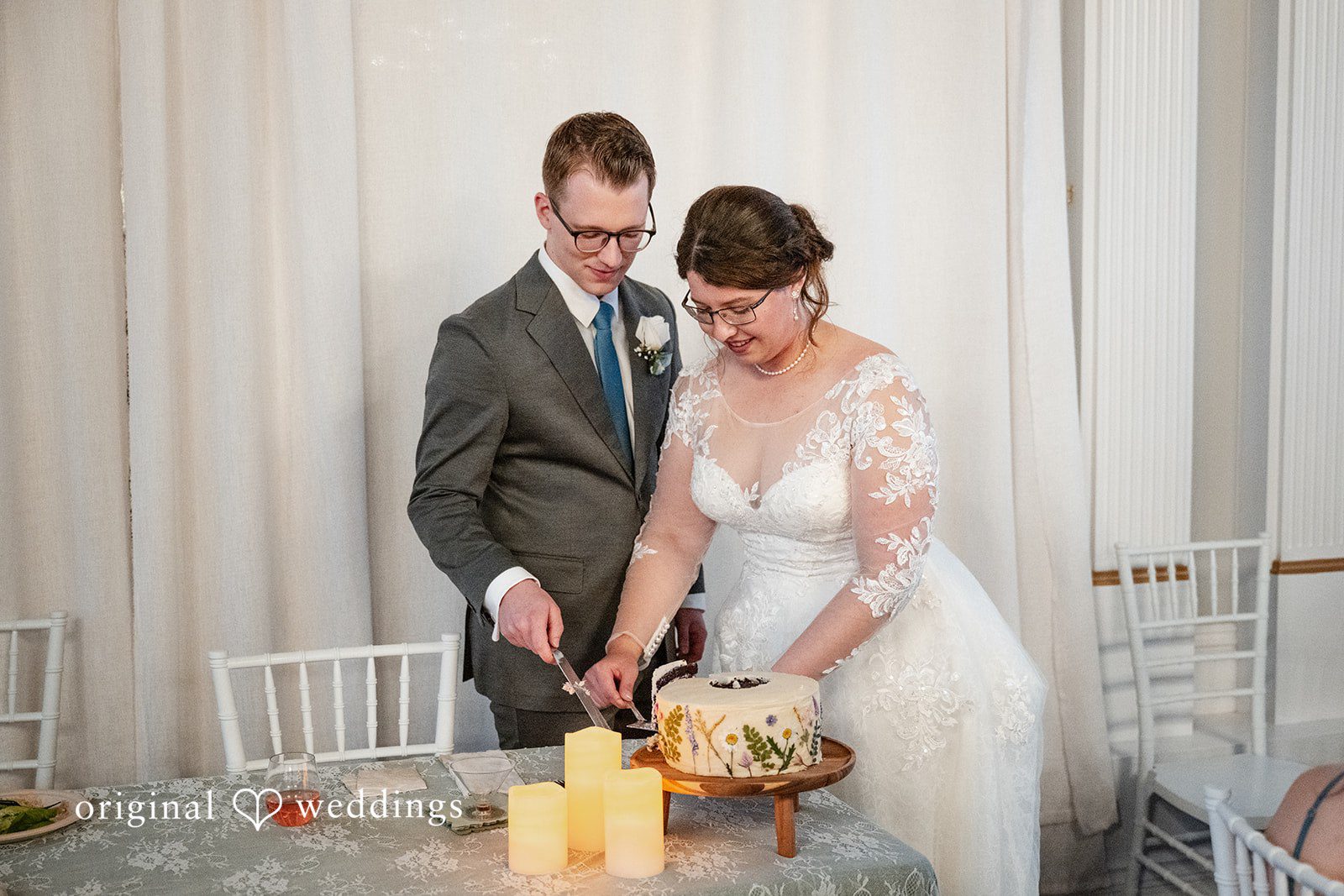 Emma + Aidan A bride and groom cutting their wedding cake together at a reception table.