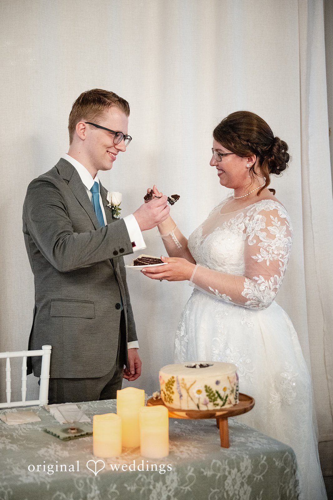 Emma + Aidan A groom offering a bite of wedding cake to his bride at the reception table.