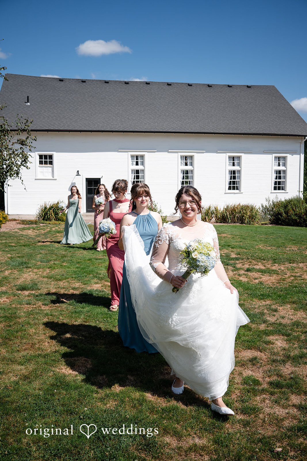 Emma + Aidan A bride running across a green lawn with a white building in the background.