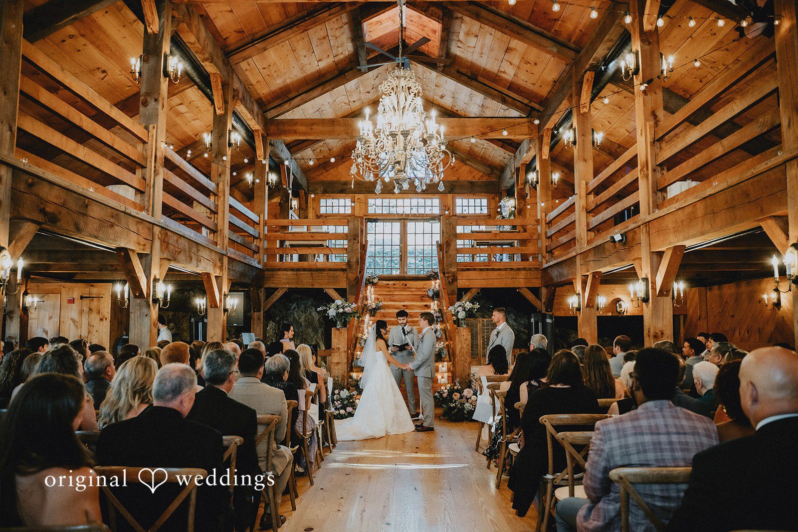 Wedding ceremony viewed from the back of a crowded chapel hall.