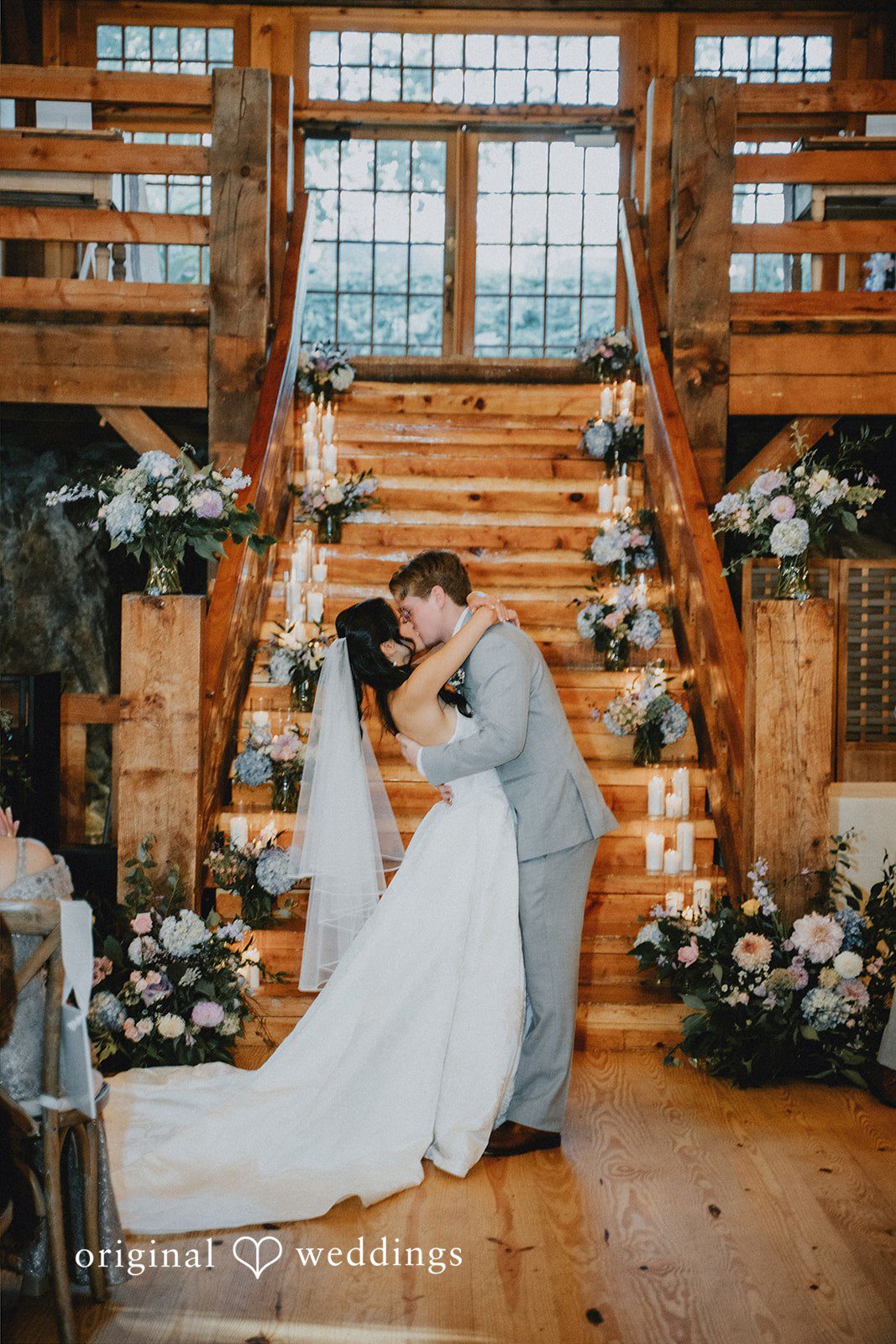 Bride and groom embracing at the bottom of a wooden staircase.
