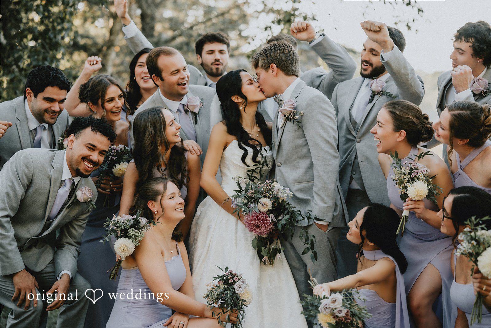 Wedding guests cheering and raising their hands in celebration around newlyweds.