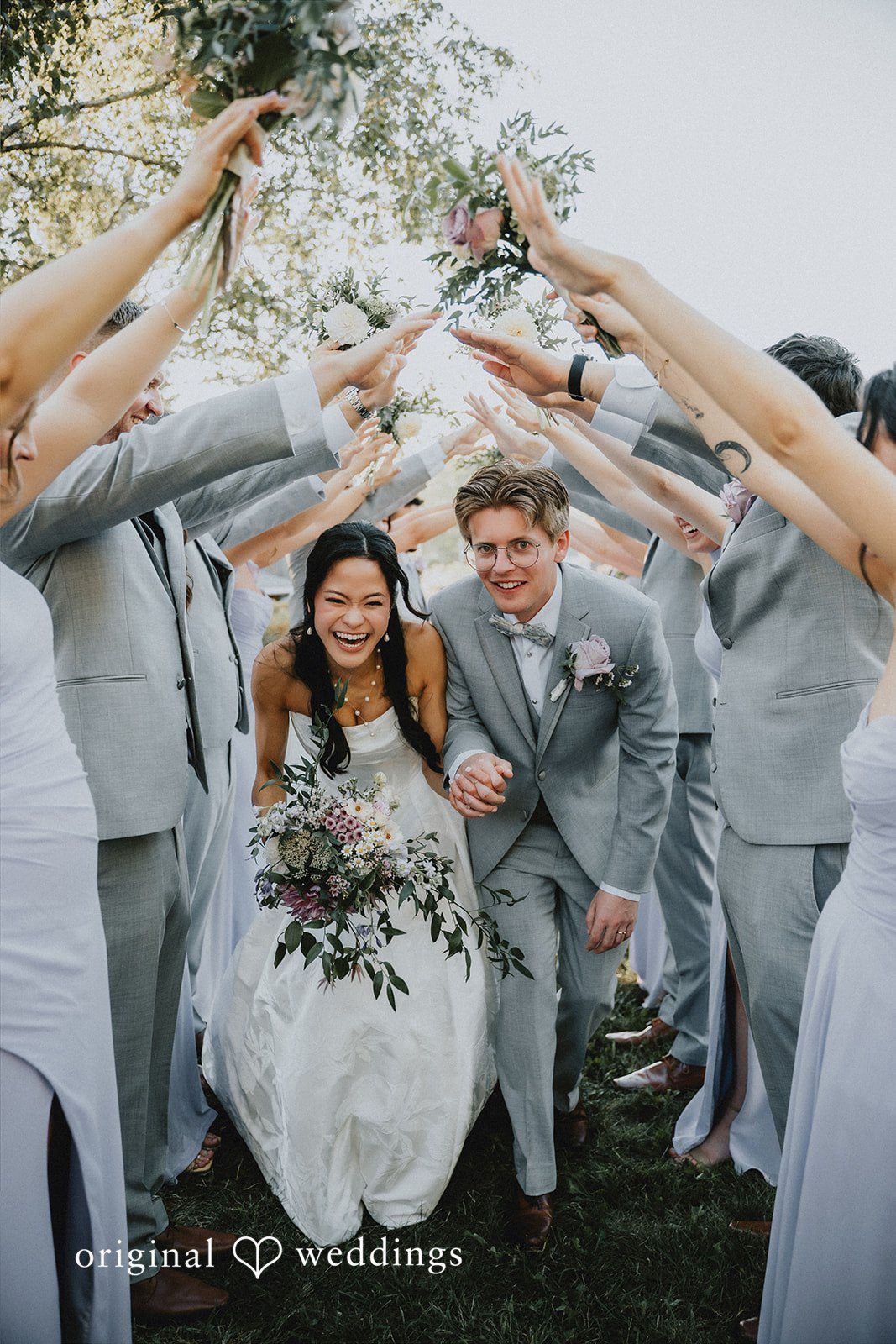 Newlyweds walking through a celebratory archway of lifted hands.