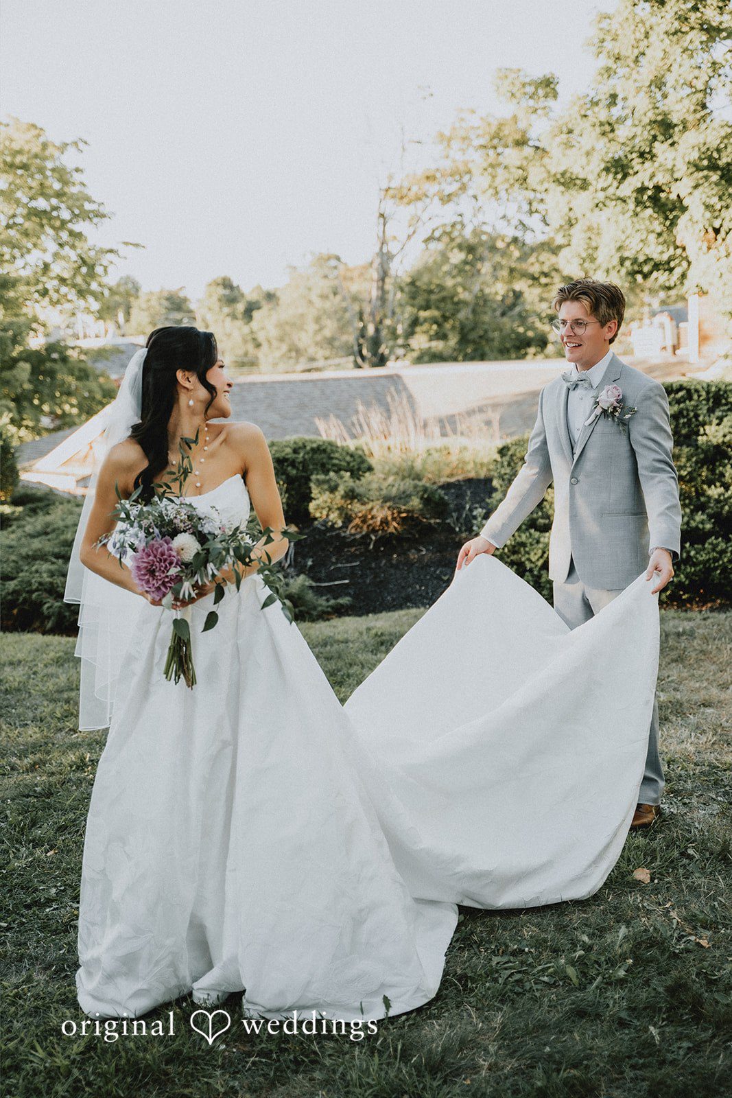 Bride and groom posing together with her long dress train spread across the lawn.