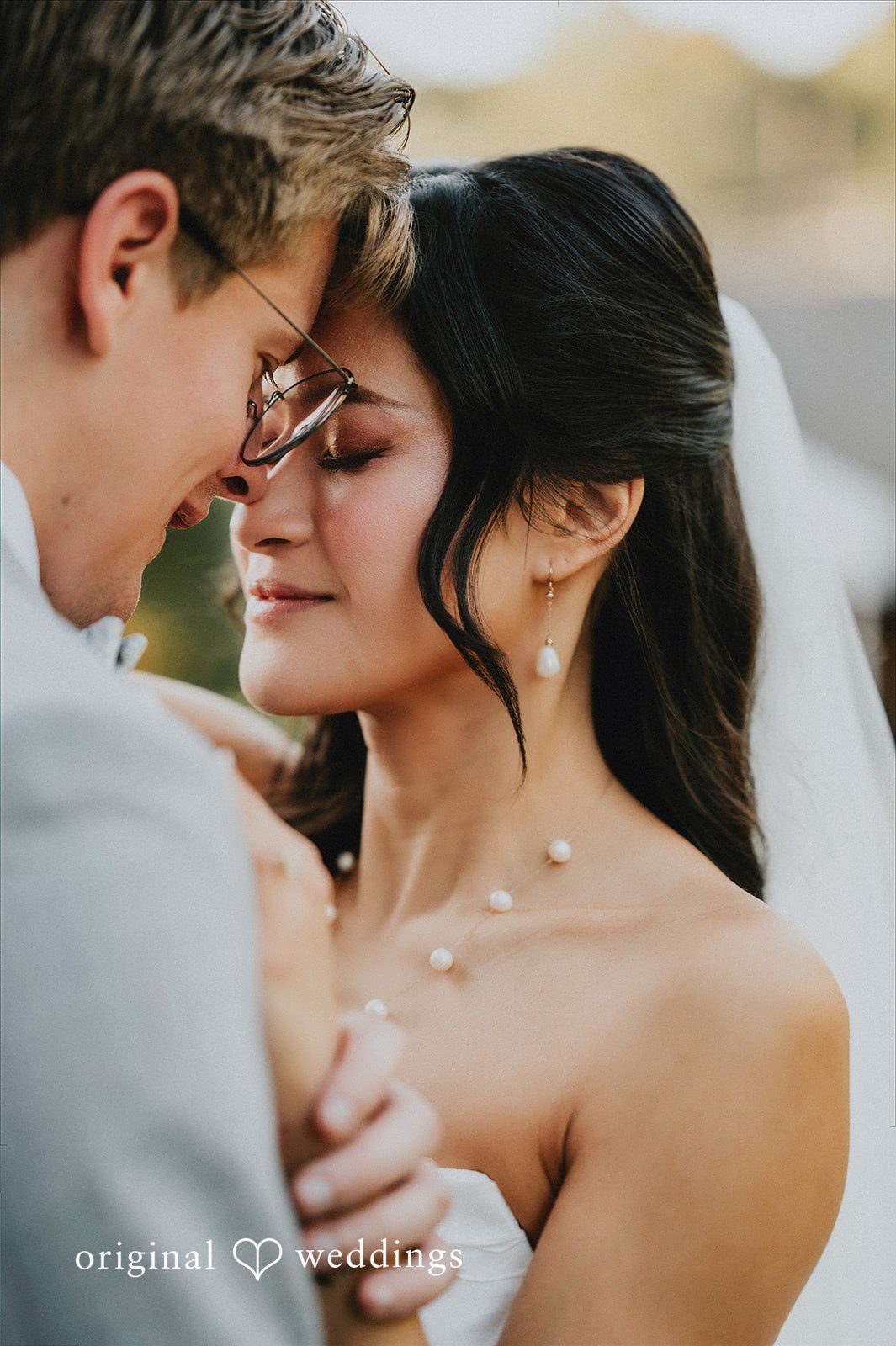 Close-up of a groom embracing a smiling bride wearing a sheer veil.