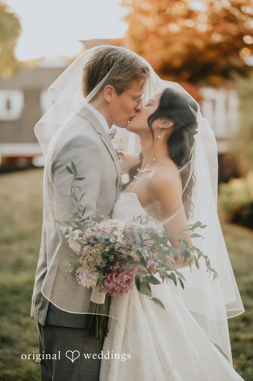 Groom kissing a smiling bride on the forehead near a building.