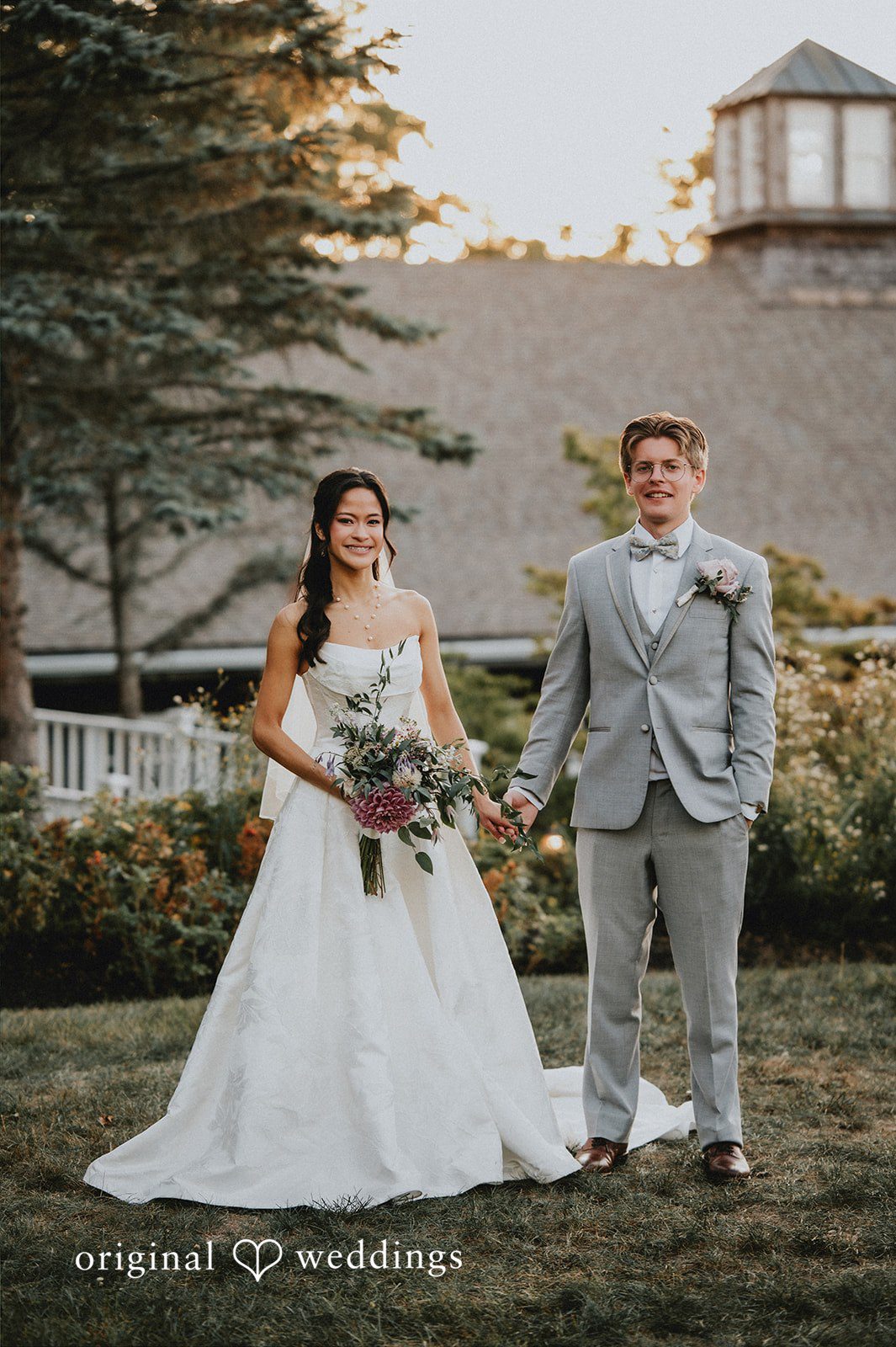 Bride and groom standing on a lawn with a building in the background.
