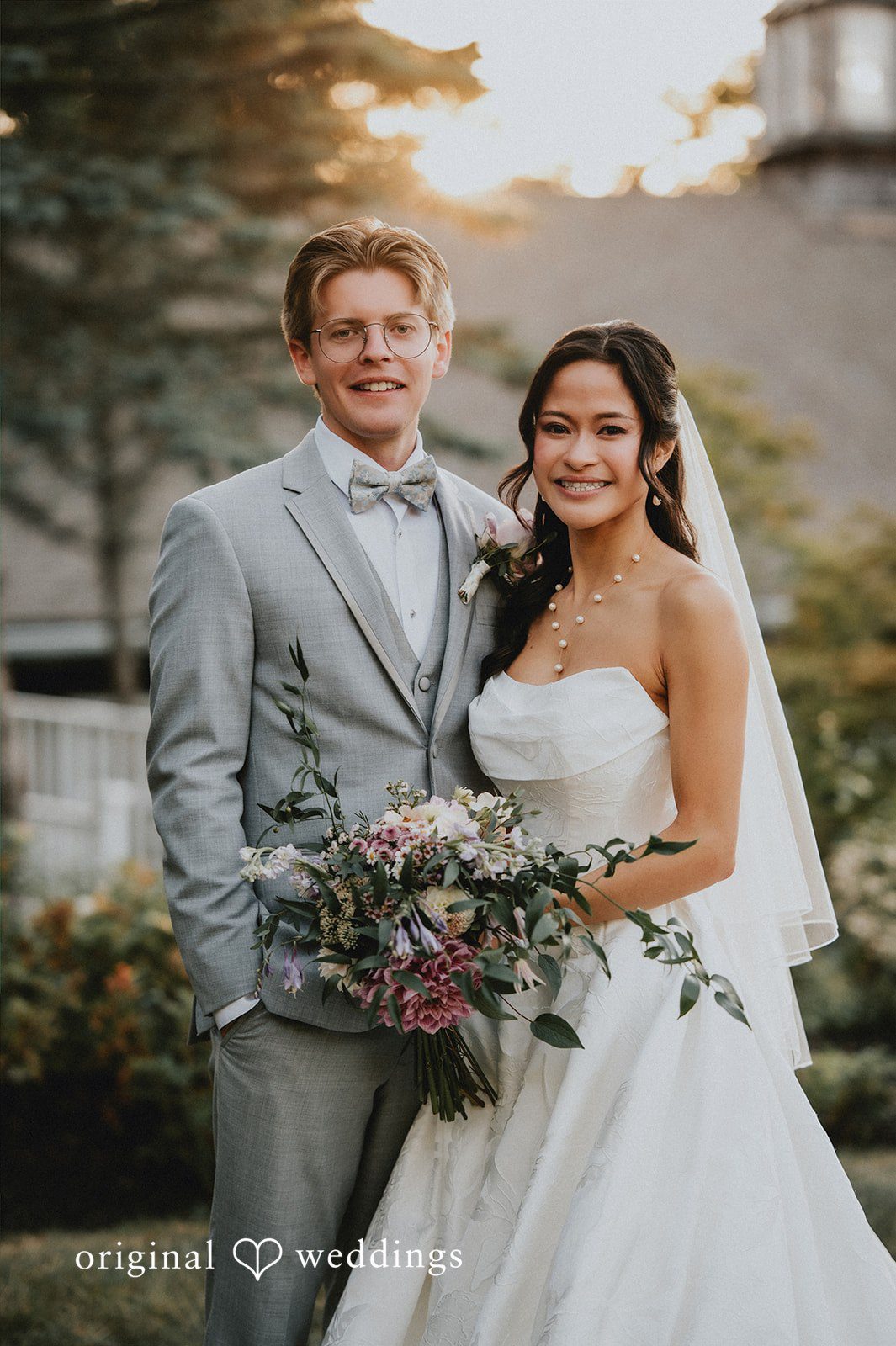 Groom in a grey suit smiling next to a bride in a white gown.