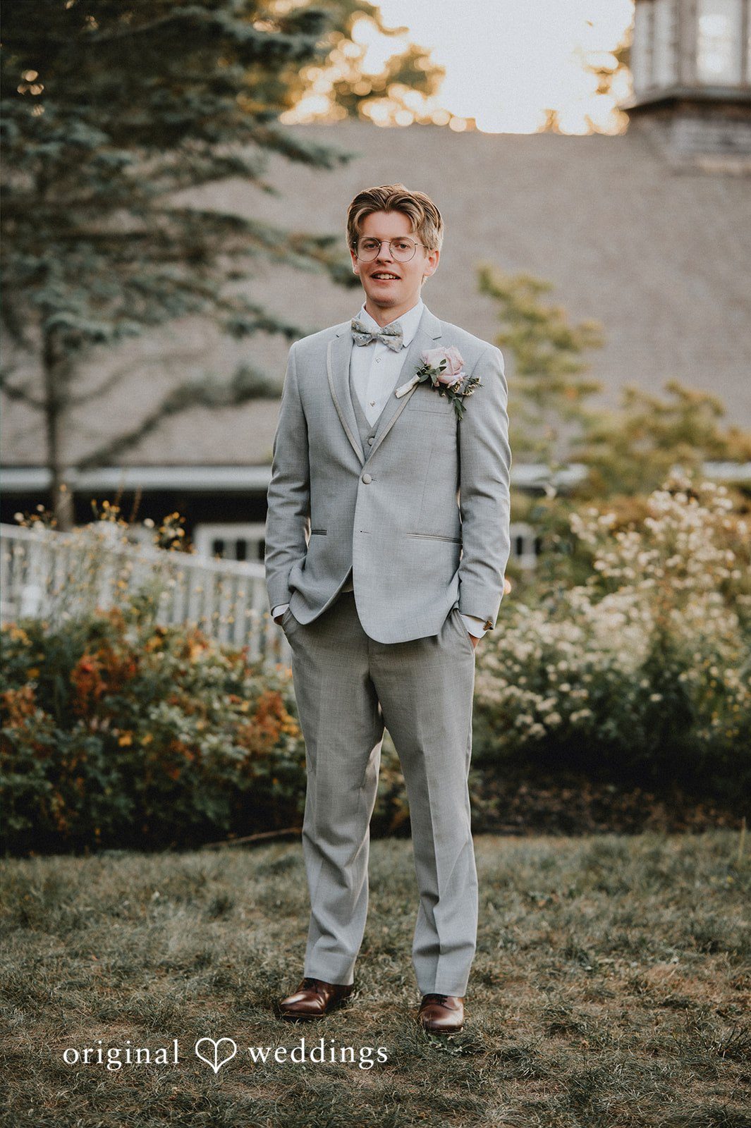 Groom in a grey suit standing on a grassy lawn.