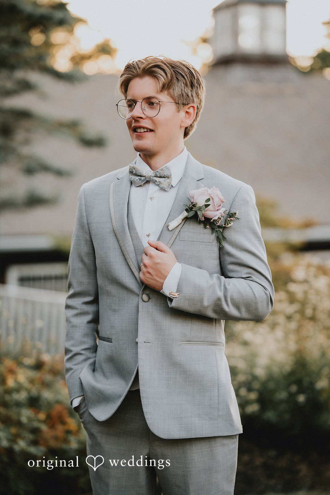 Groom wearing a light grey suit and bowtie smiling.