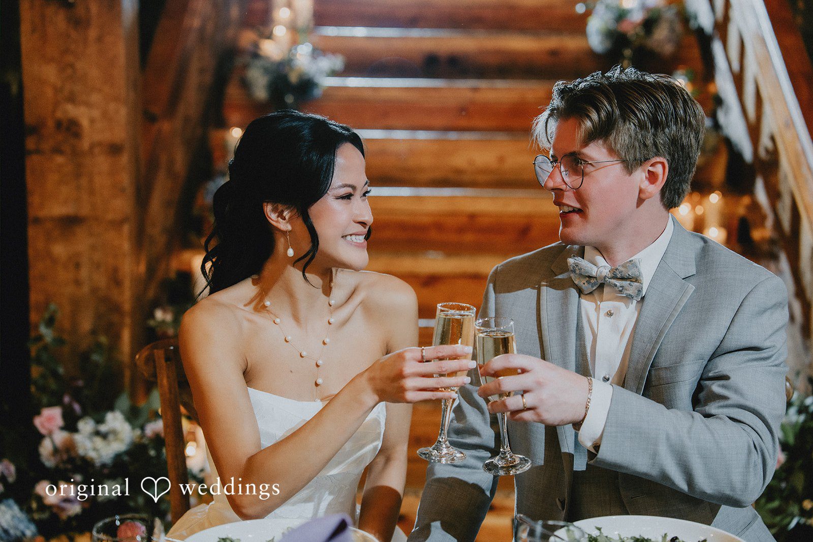 Bride and groom clinking glasses together while sharing a laugh at their reception.