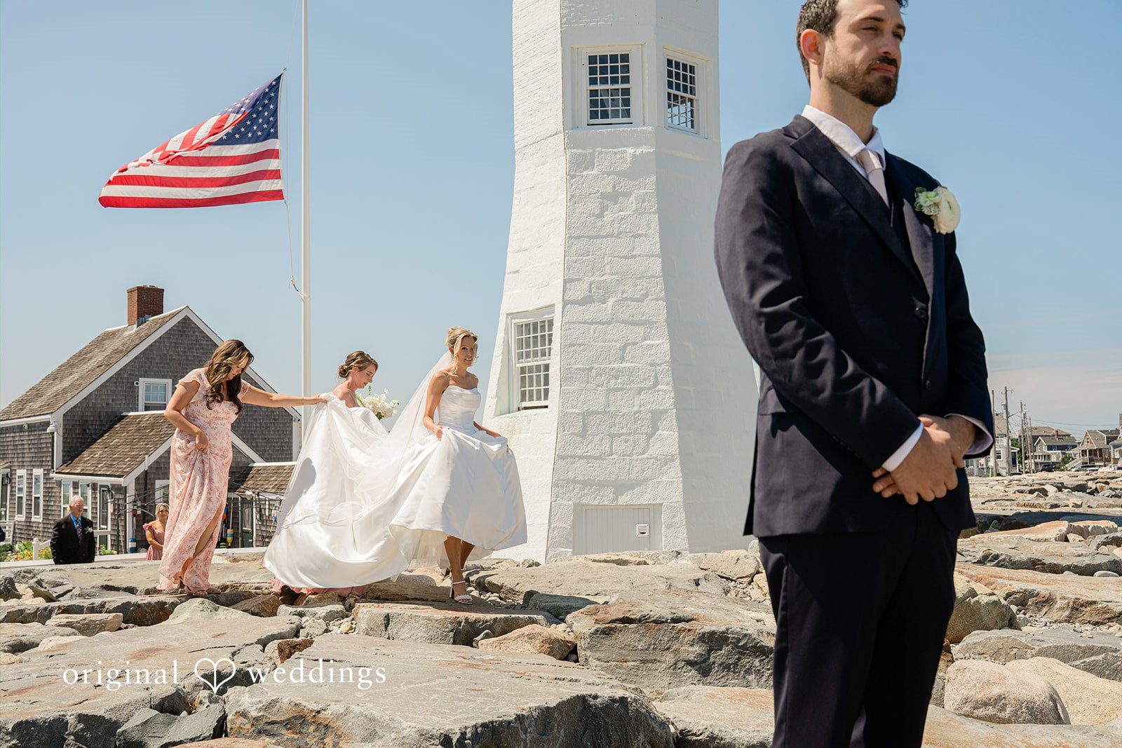 Jessica + Keegan A wedding party posing for a photo near a coastal lighthouse.