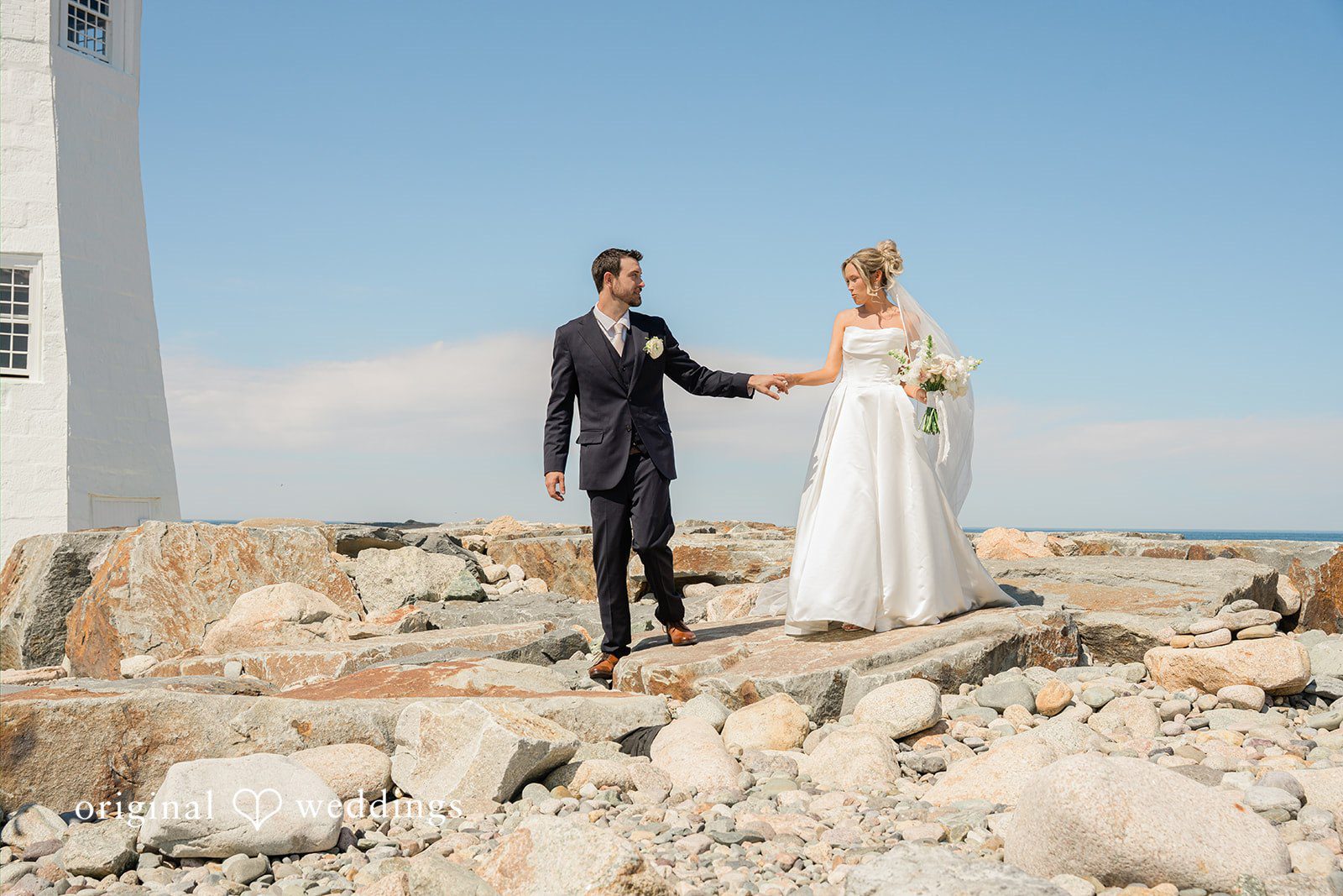 Jessica + Keegan A bride and groom walking hand-in-hand along a scenic rocky coastline.
